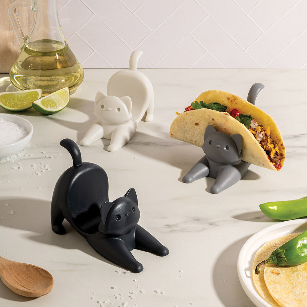 Cat-shaped taco holders on a kitchen counter with food and kitchen items.